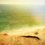 Photographie d'une plage au sable doré. L'océan atlantique avec des reflets vert et jaune.