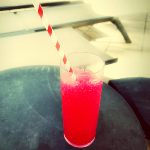 Photographie d'une verre remplit d'une boisson rouge glacé à la framboise avec une paille rouge et blanche