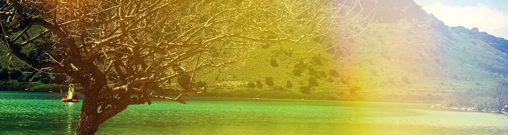 Photographie du lac de Kournas en Crète. L'eau du lac a des teinte de bleu turquoise, de jaune et de vert. La montagne aride en arrière plan.