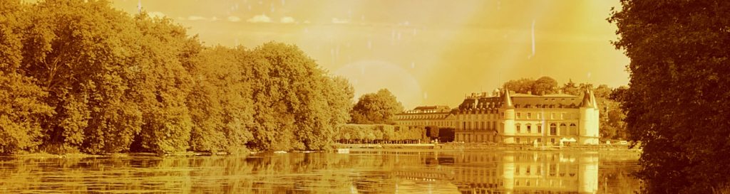 Photographie du château de Rambouillet prise au fond du parc. Le château au loin se reflète sur les eaux tranquilles du lac.