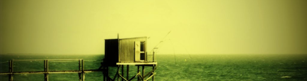 Photographie d'une pêcherie en bois au bord d'une plage. L'océan aux reflets verts entoure le cabanon.