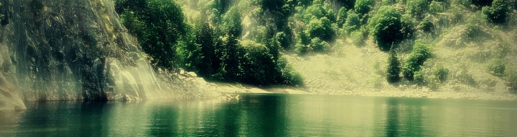 Photographie d'un lac de montagne entouré par les montagnes couvertes de sapins verts foncés et des rochers blancs.
