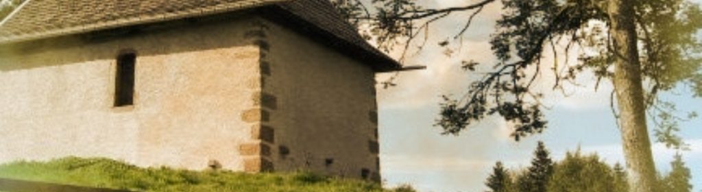 Photographie d'une chapelle construite au bord du lac de Longemer sur une petite colline entourée de sapins verts.