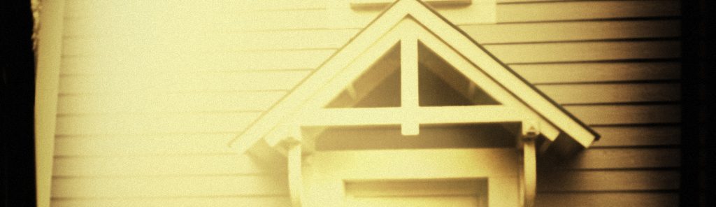 Photographie d'une maison blanche en bois hantée par des esprits mystérieux. Elle se tient, dressée, dans les bois près d'un lac bordé de roseaux et recouvert par la brume.