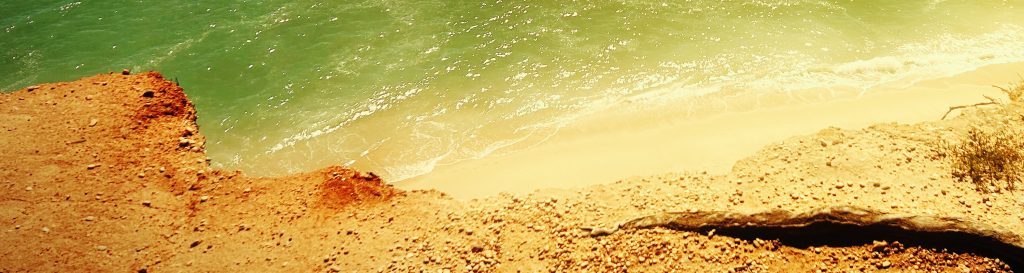 Photographie d'une plage au sable doré. L'océan atlantique avec des reflets vert et jaune.