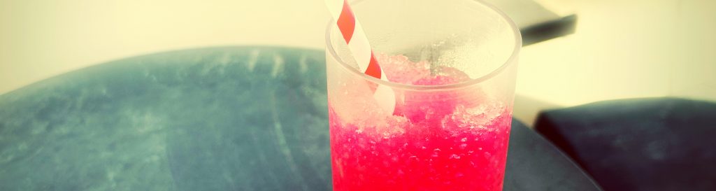 Photographie d'une verre remplit d'une boisson rouge glacé à la framboise avec une paille rouge et blanche.