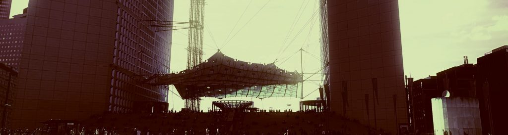 Photographie de la grande arche de la Défense avec le soleil qui se reflète sur la structure.