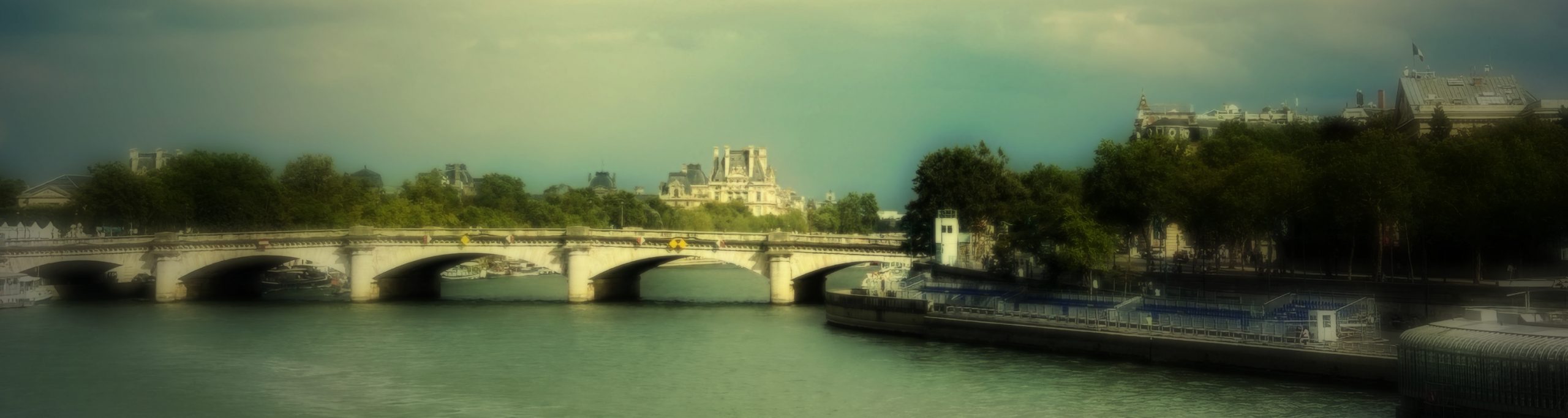 Photographie d'une vue sur le pont de la Concorde à Paris. La Seine en premier plan, des péniches et des arbres bordent les rives.