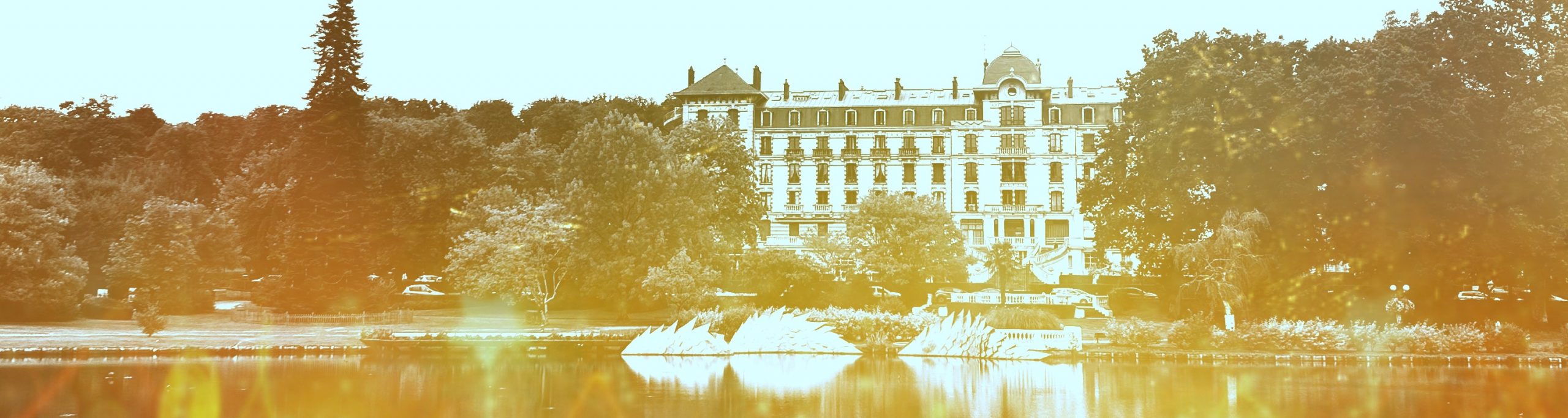 Photographie des termes de Bagnoles de l'Orne. Au premier plan le lac et au fond les termes entouré d'arbres.