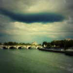 Photographie d'une vue sur le pont de la Concorde à Paris. La Seine en premier plan, des péniches et des arbres bordent les rives.